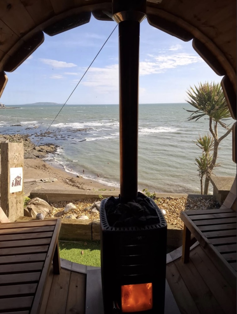 View from inside the barrel sauna: the wood stove glows in the foreground and the sea and Ireland's Eye fill the window
